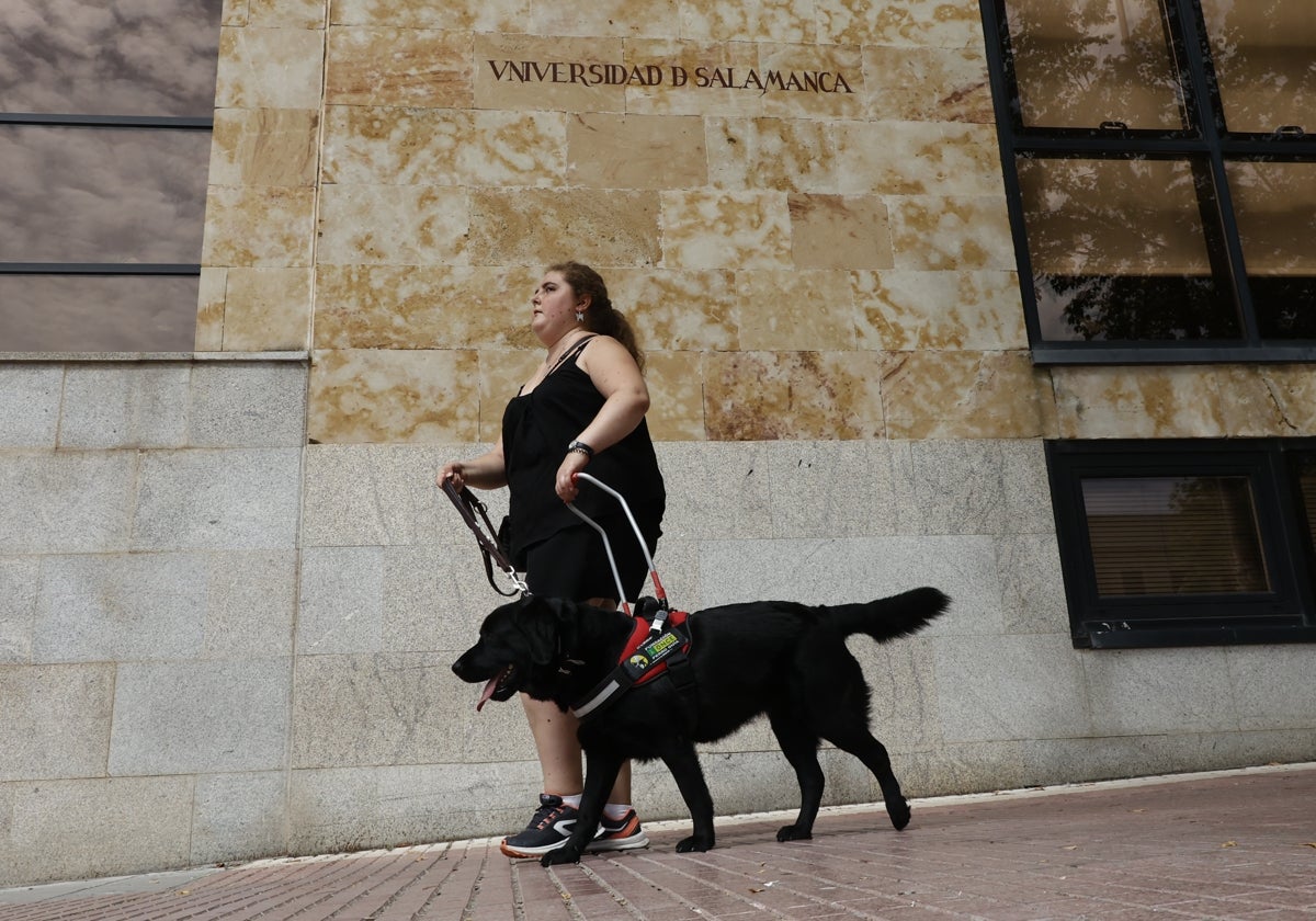 La joven invidente Claudia Iturregui con Miel, su perra guía, por la fachada de la Facultad de Derecho.