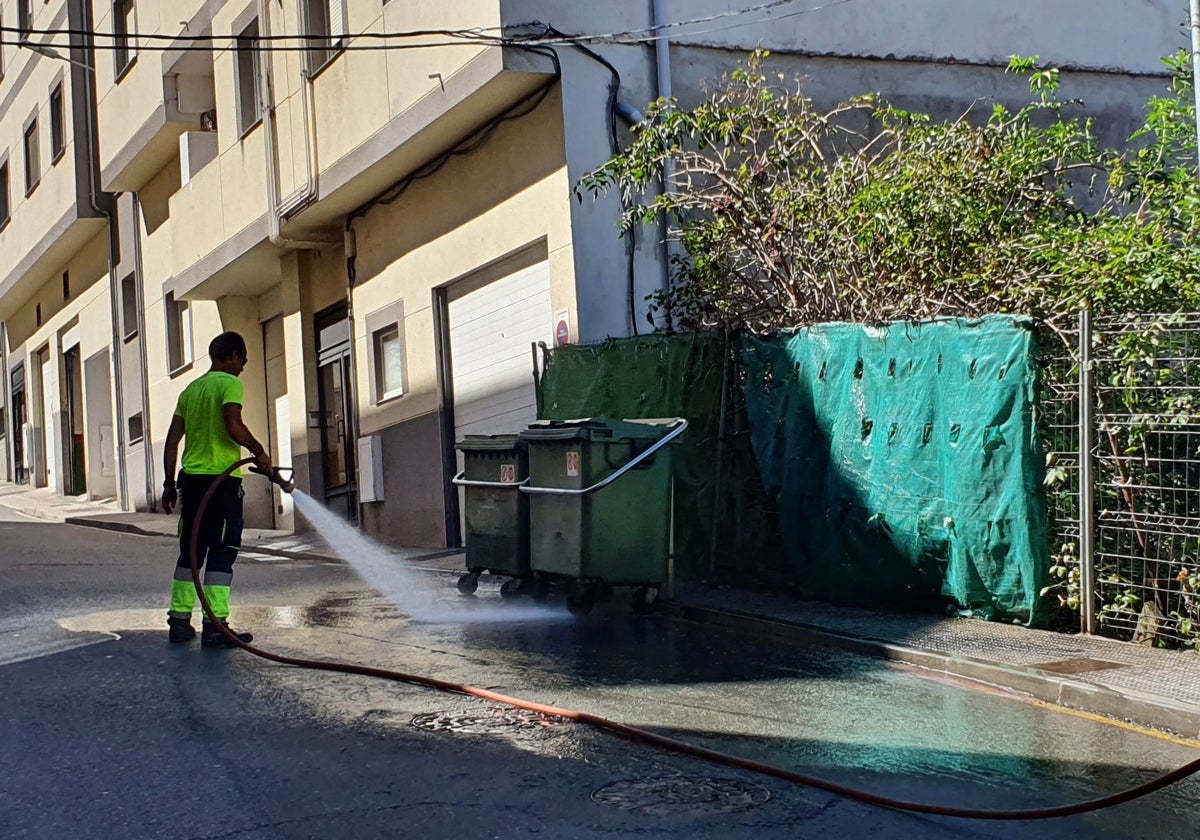 Imagen de un operario de limpieza retirando con agua la suciedad acumulada en ese tramo del acerado.