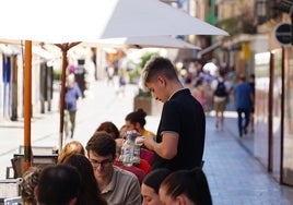 Un joven atiende a los clientes de una terraza del centro de Salamanca.