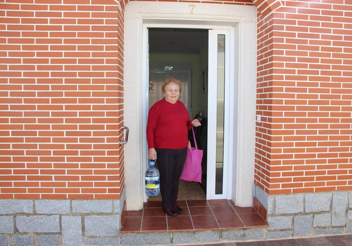 Una vecina entra en su hogar con una garrafa de agua que ha adquirido en la tienda a la vez que ha realizado la compra del pan diario.