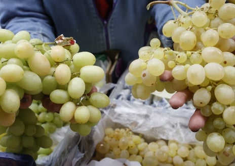 Imagen secundaria 1 - La frutera Susana Sánchez atiende a un cliente en su puesto en el mercado central. Los precios de las uvas con y sin pepitas.