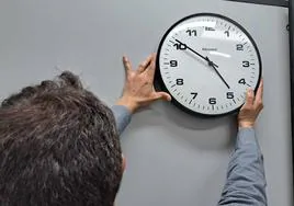 Un joven descuelga reloj de pared para adelantar la hora.