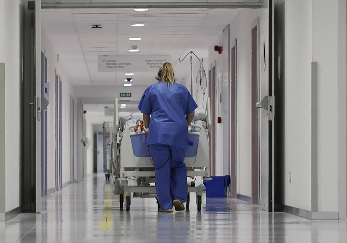 Una celadora del Hospital transporta a un paciente en camilla a lo largo de un pasillo.