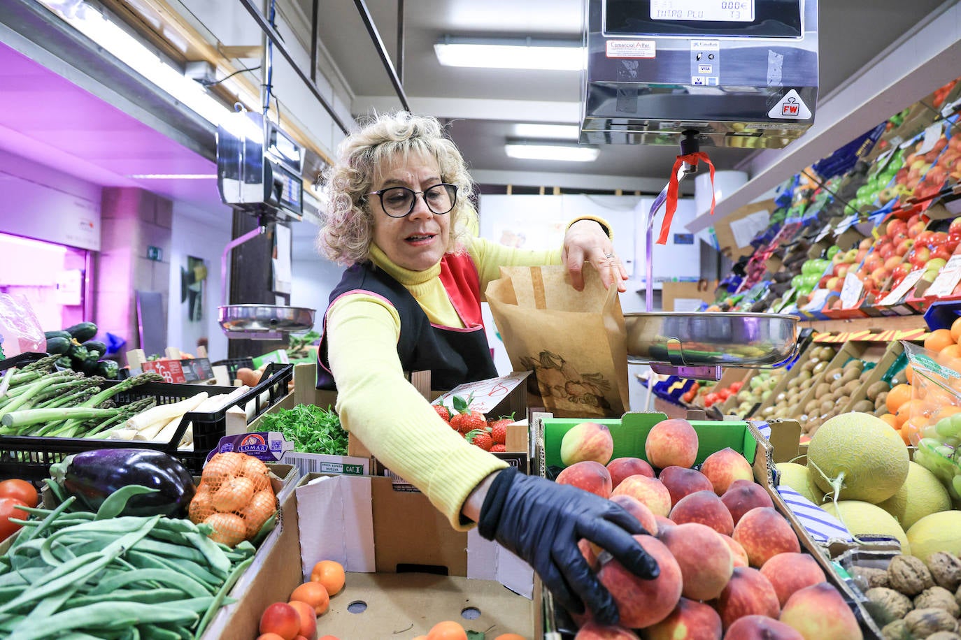 Una frutera del Mercado Central escoge algunos melocotones para vendérselos a una clienta.