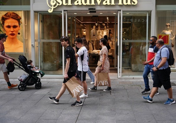 Varias personas con bolsas ante las puertas de una tienda.