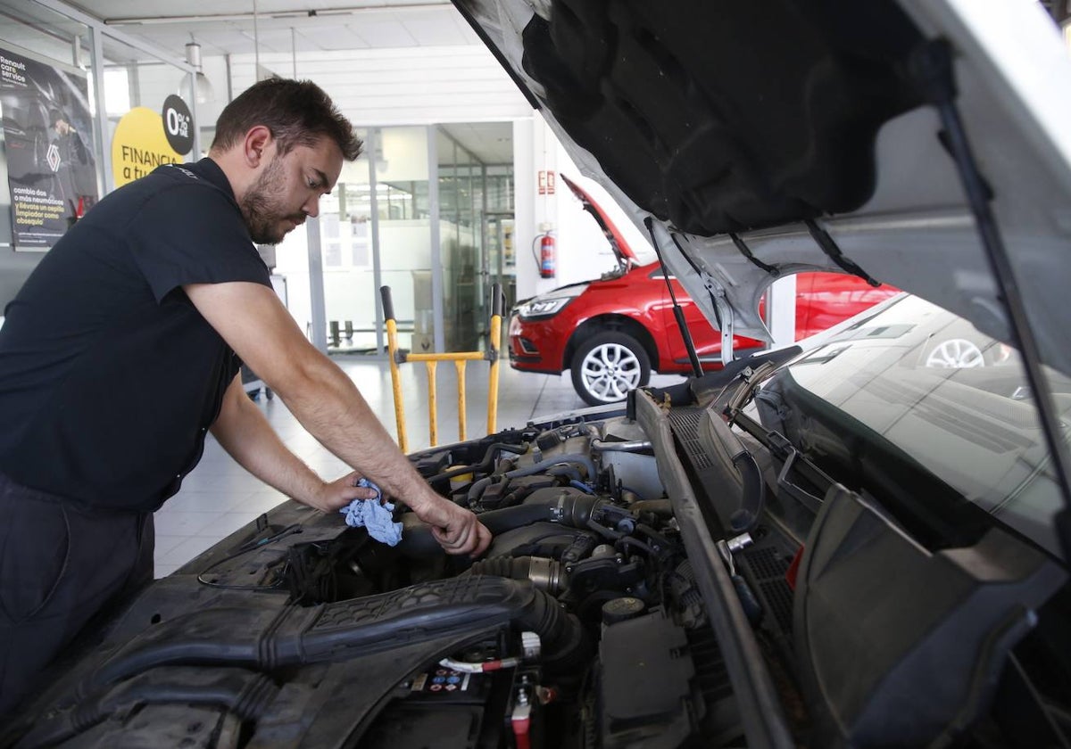 Un hombre trabaja el motor de un coche en un taller de la ciudad