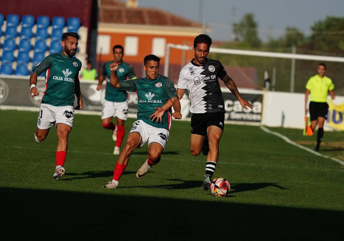 Álvaro Gómez conduce el cuero ante dos rivales.