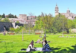 Varios grupos toman el sol y pasan la tarde al lado del Puente Romano y con las catedrales de fondo.