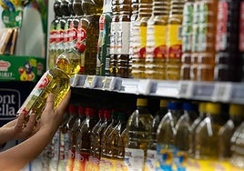 Una persona agarra una botella de aceite de oliva en un supermercado.