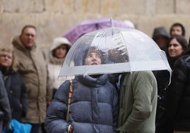 Dos jóvenes se refugian de la lluvia bajo un paraguas.