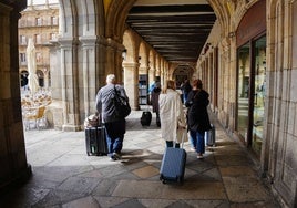 Viajeros con maletas por los soportales de la Plaza.