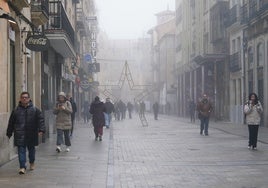 Personas pasean abrigadas para combatir el frío y la niebla por la calle de la Rúa.