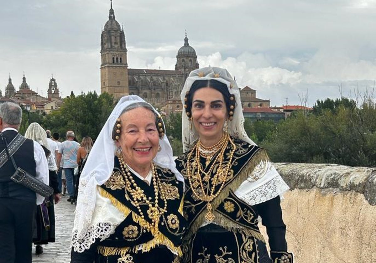 Dos mujeres de Macotera lucen su traje charro moderno sobre el Puente Romano de Salamanca, con las catedrales al fondo.