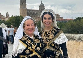 Dos mujeres de Macotera lucen su traje charro moderno sobre el Puente Romano de Salamanca, con las catedrales al fondo.