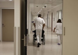 Un trabajador del Hospital traslada a un paciente en silla de ruedas.