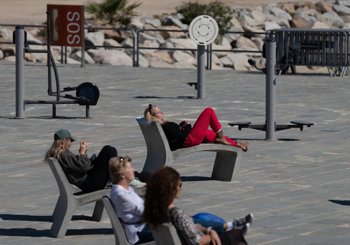 Varias personas toman el sol en el paseo marítimo de la playa del Bogatell |