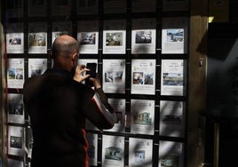 Un hombre saca una fotografía de los anuncios de pisos en una inmobiliaria salmantina.