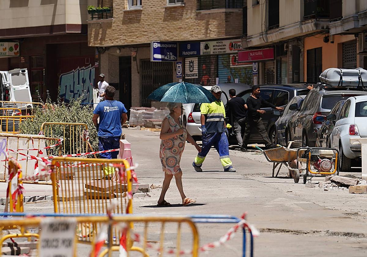 Varios obreros de construcción trabajan bajo el sol mientras una vecina se refugia bajo una sombrilla.