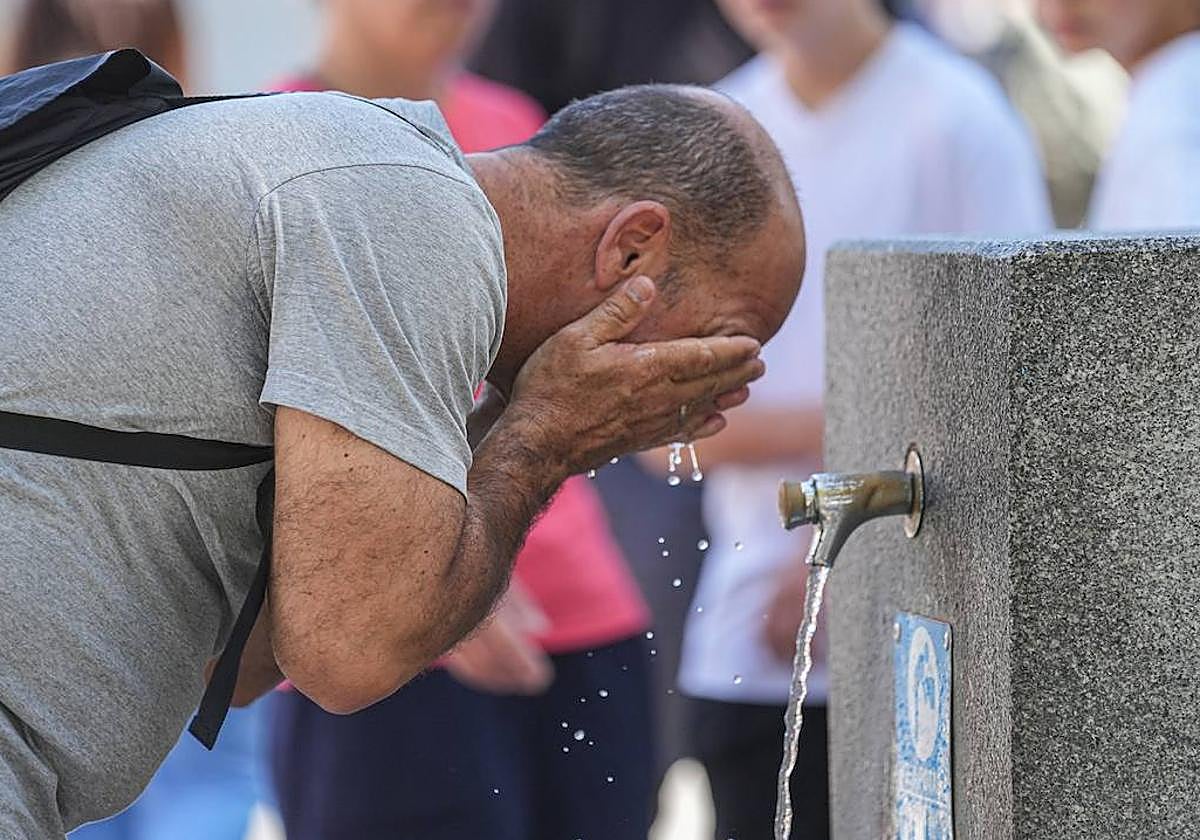 Un hombre se refresca en fuente pública.