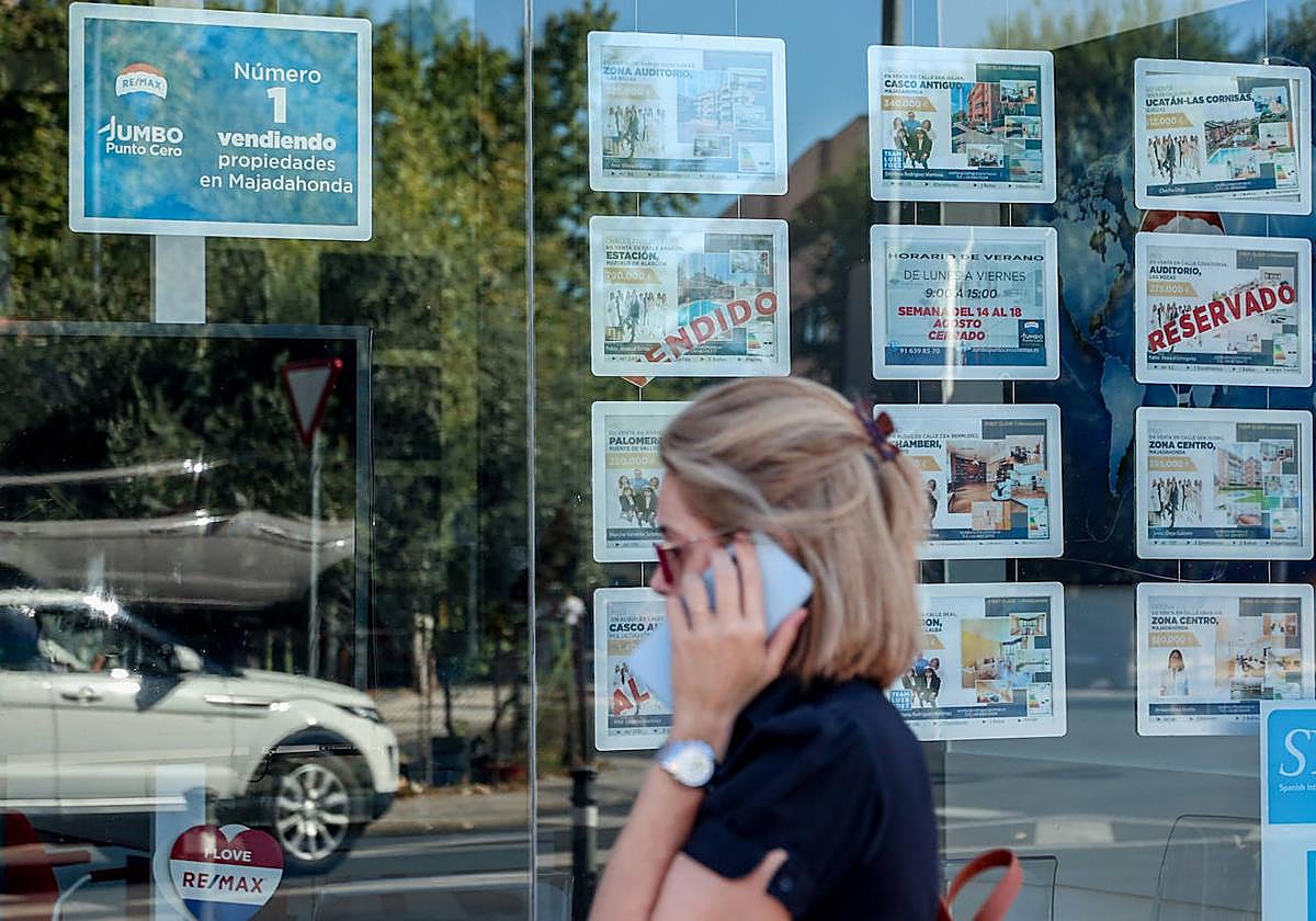 Una mujer camina frente a un escaparate de anuncios de viviendas, en Madrid.