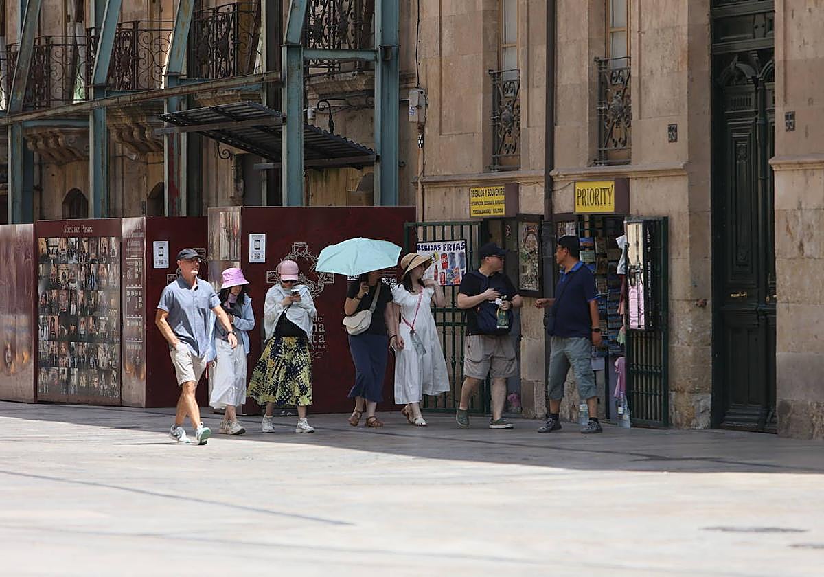Varias personas se protegen del calor en Salamanca con gorras y paraguas.