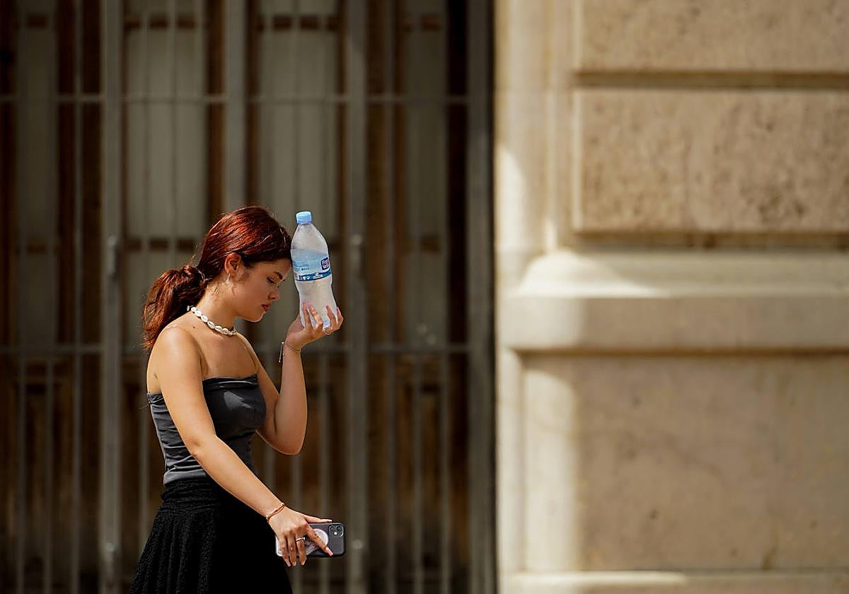 Una joven combate el calor poniéndose una botella de agua fría en la frente.