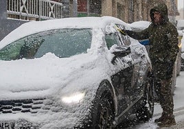 Un hombre intenta quitar la nieve de su vehículo.