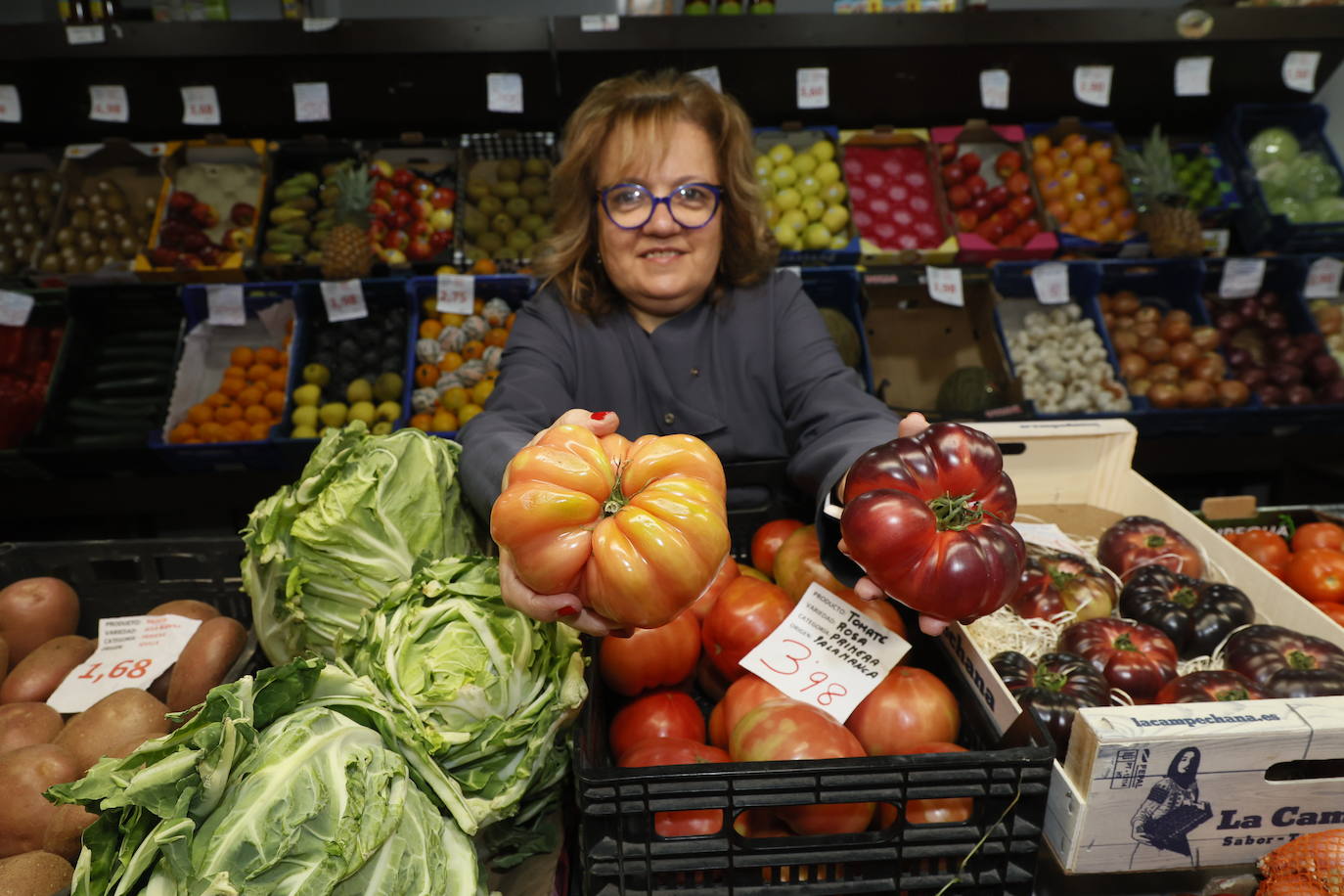 Una frutera del Mercado, cogiendo un tomate rosa y un tomate azul en su estand.