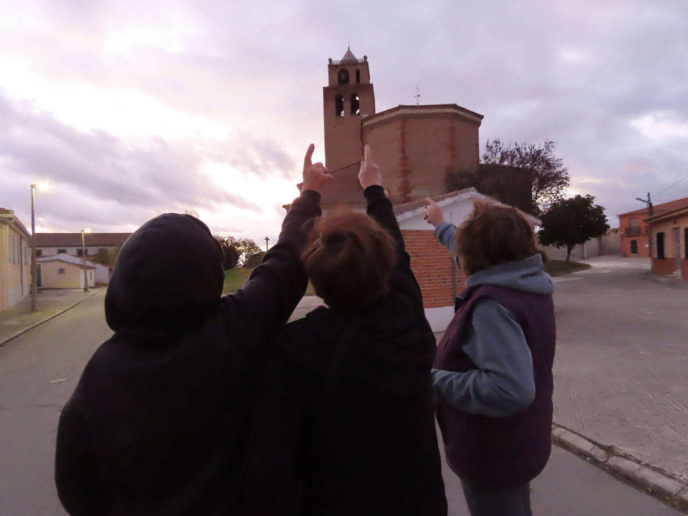 Tres mujeres señalan a lo alto de la torre de la iglesia de San Miguel Arcángel, de Zorita de la Frontera, donde se ve la cúpula de hormigón que quieren retirar en las labores de restauración.