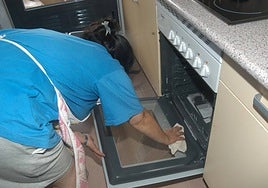 Una empleada de hogar limpia el horno de la cocina de una vivienda.
