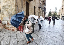 Varias personas, protegiéndose del aire, del frío y de la lluvia en el centro de Salamanca.