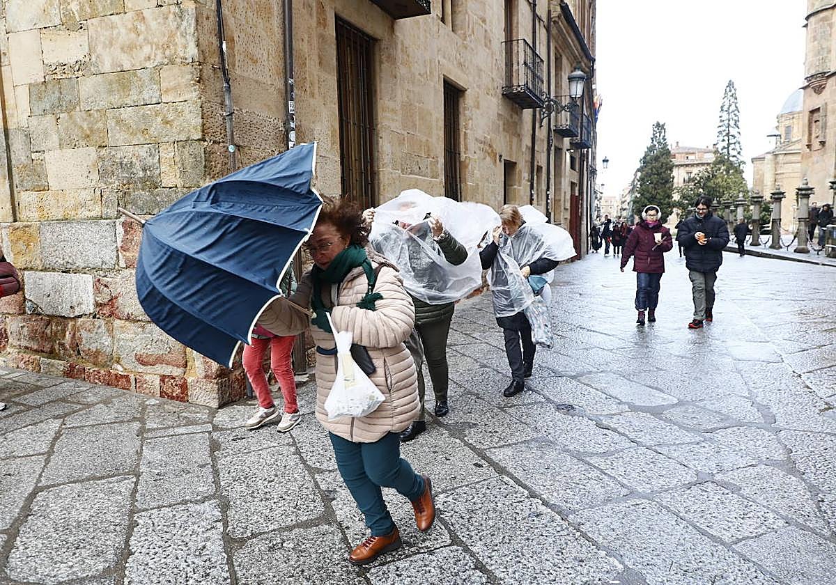 Varias personas, protegiéndose del aire, del frío y de la lluvia en el centro de Salamanca.