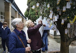 Dos mujeres colocan un mensaje para sus seres queridos en el árbol instalado en el cementerio.