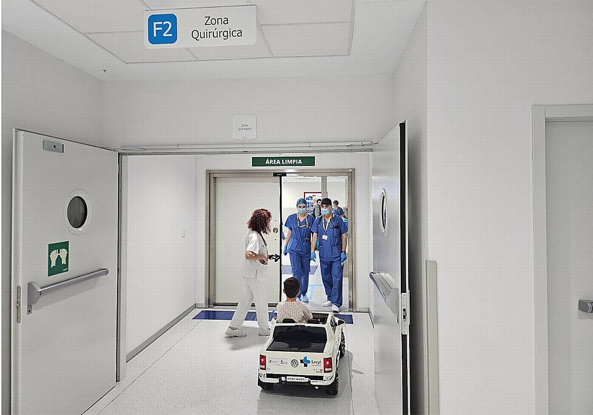 Imagen de un menor, junto a su acompañante, llegando al área quirúrgica del Hospital en un coche eléctrico.