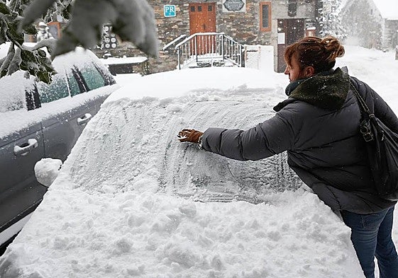 Una mujer intenta quitar la nieve de un coche.