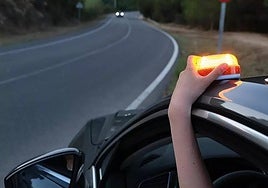 Una persona, colocando una baliza V-16 en su vehículo.