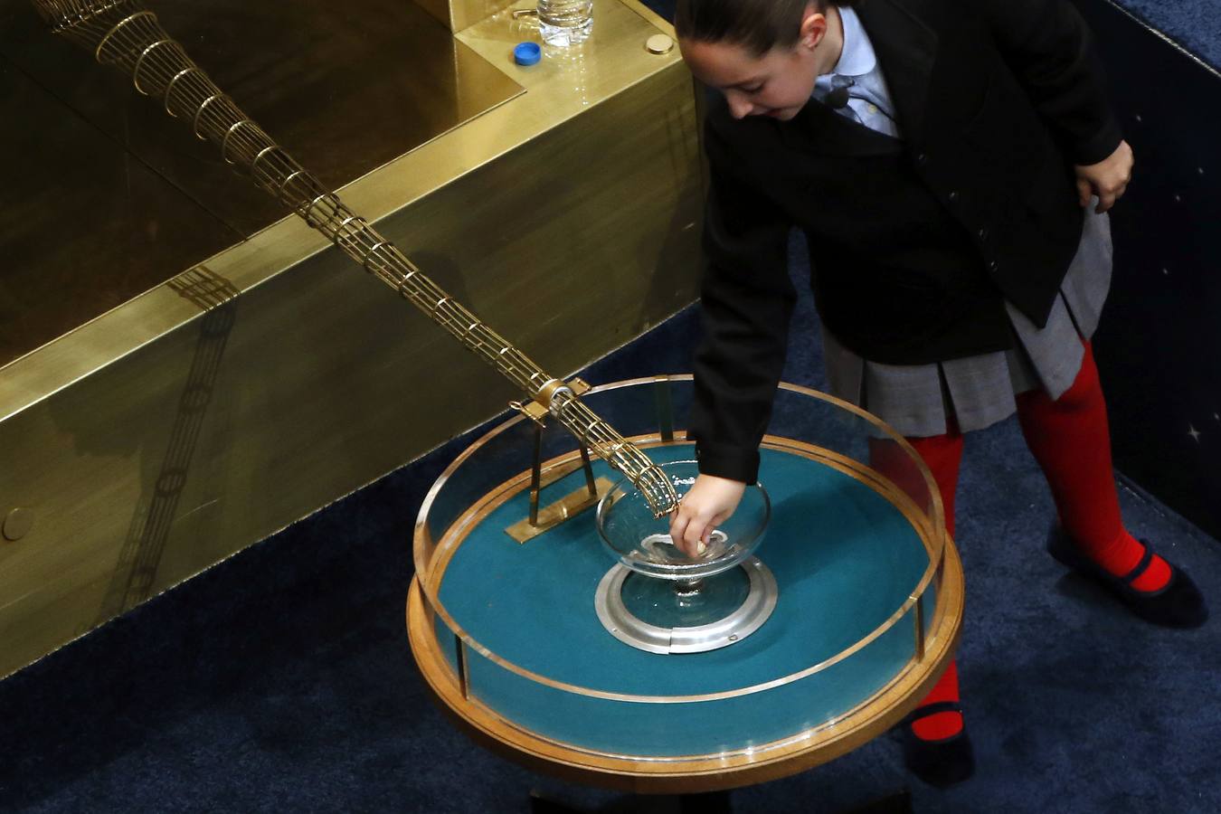 Una niña del colegio de San Ildefonso recoge una bola tras caer del bombo en el sorteo de la lotería de Navidad.