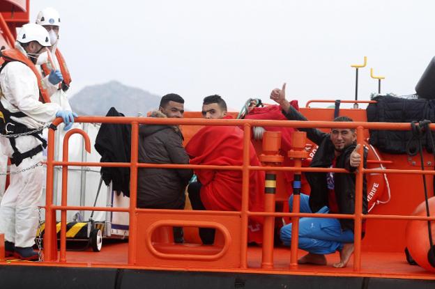 Tres inmigrantes saludan desde la patrullera Guardamar Calíope ante la mirada de miembros de Salvamento Marítimo. :: pablo sánchez / agm