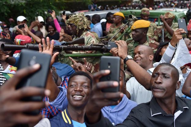 Un grupo de jóvenes se hace selfis con miembros de las fuerzas de seguridad de Zimbabue de fondo durante la manifestación de ayer. 
