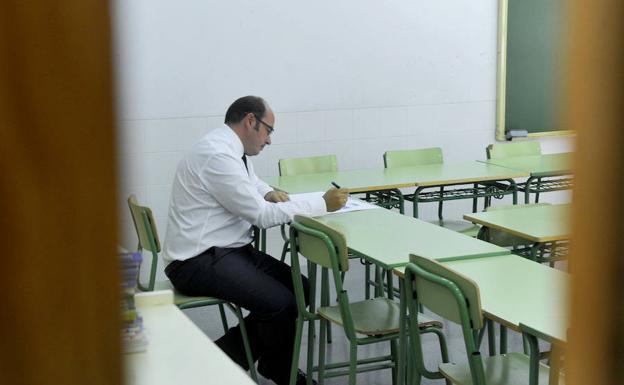 Un profesor corrige unos exámenes en un aula. 