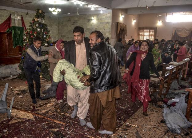 Varios hombres se llevan a heridos tras el atentado durante la preparación de los actos de Navidad dentro del templo de Quetta, en Pakistán. :: A. CALVIN / AFP