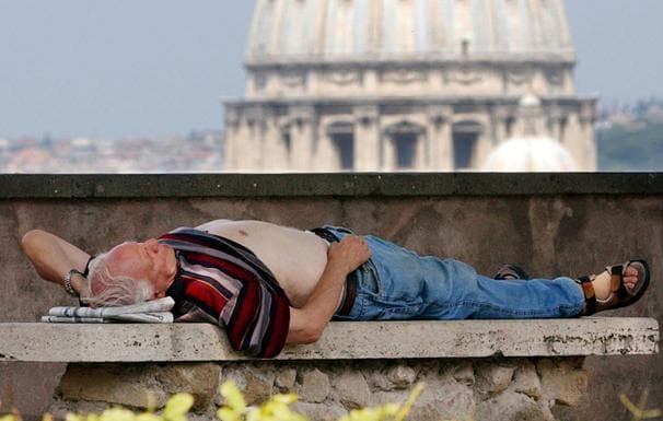 Un hombre descansa en un banco con vistas a la Basílica de San Pedro. 