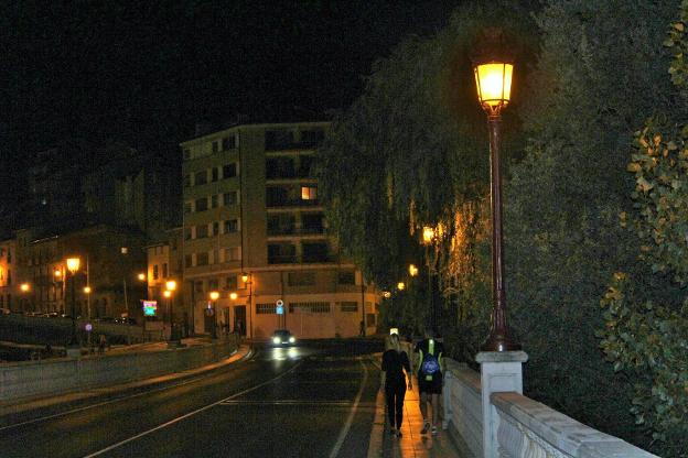 Una pareja camina por el puente iluminado sobre el Tirón. :: D.M.A.