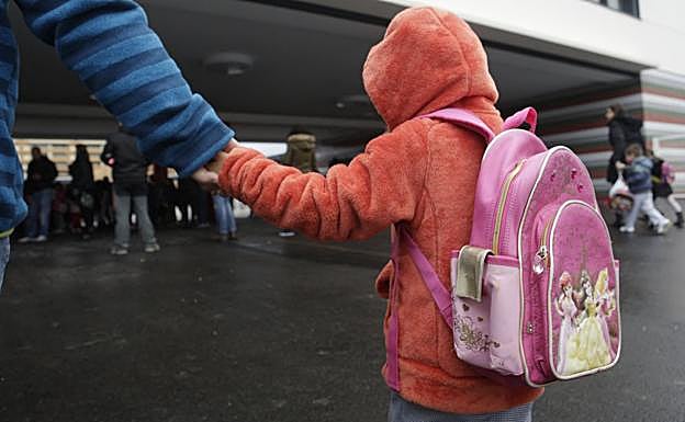 Una niña camina por la calle de la mano de un adulto. 