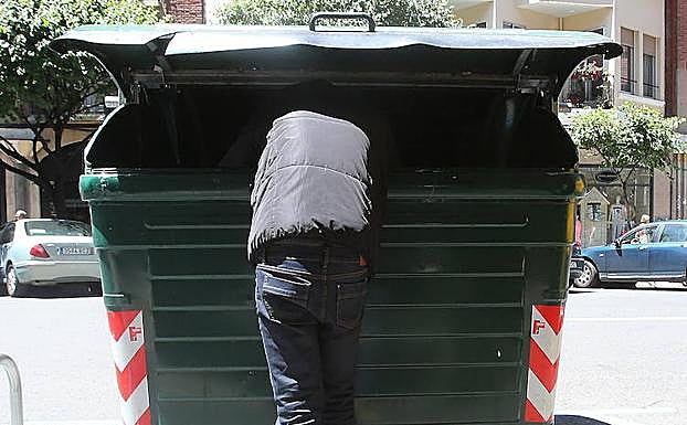 Una persona sin hogar, rebuscando en un contenedor. 