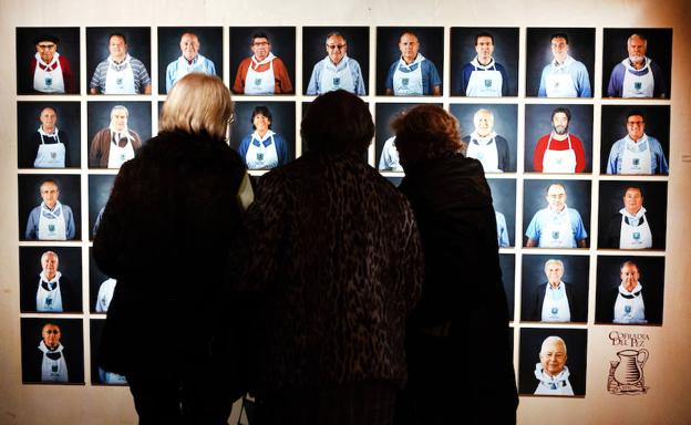 Tres visitantes observan las fotografías de los actuales miembros, tanto de número como honorarios, de la Cofradía del Pez. :: 