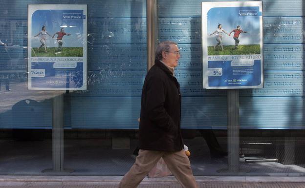 Un hombre camina frenta a un escaparate donde se anuncian planes de pensiones.