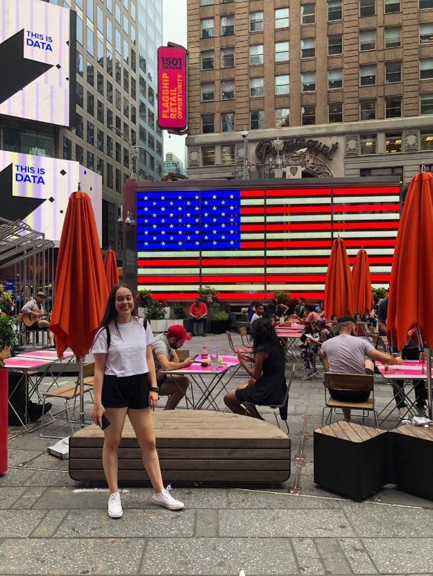 Ana en Times Square frente a la bandera de Estados Unidos.