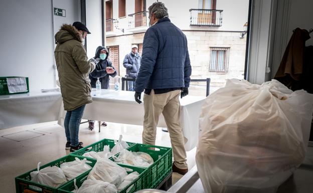 Dos voluntarios, junto a una caja llena de bolsas con alimentos. 