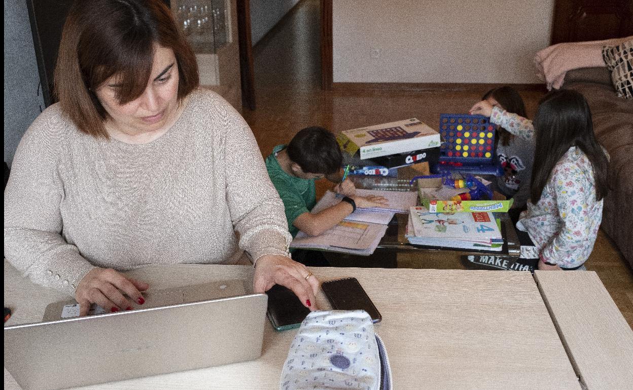 Una madre trabaja desde casa mientras sus hijos estudian al lado.